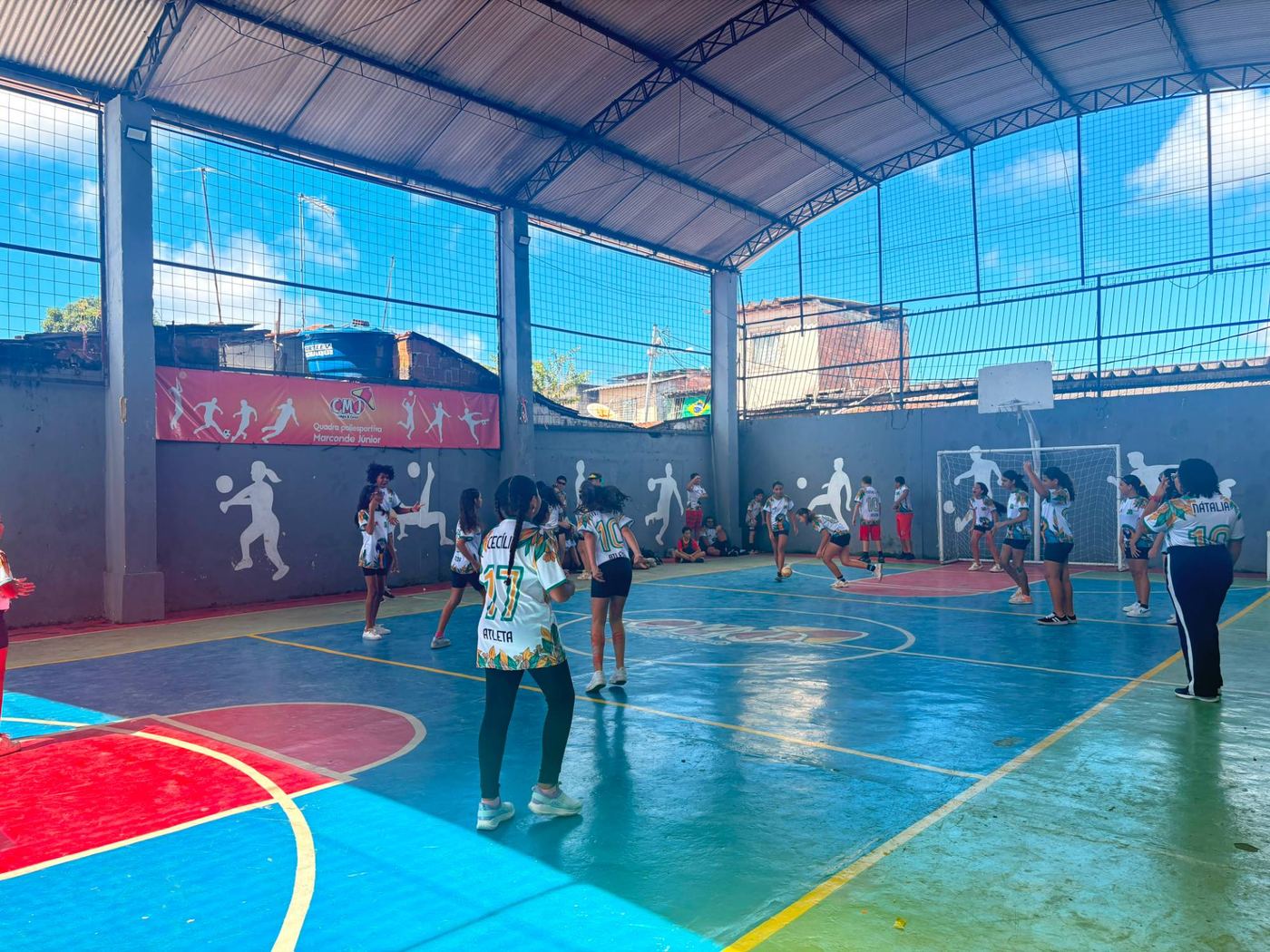 Estudantes do CMJ jogando futebol na quadra poliesportiva coberta Marconde Júnior, com desenhos de atletas nas paredes