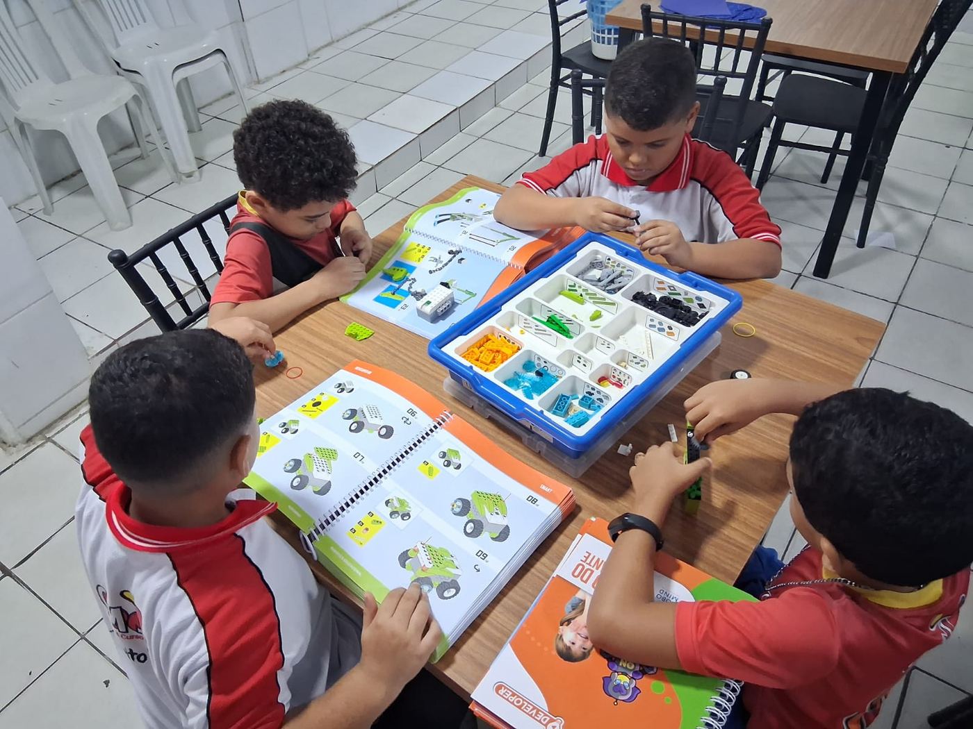 Quatro estudantes do CMJ de uniforme montando um robô com peças de encaixe, com os manuais de montagem abertos na mesa