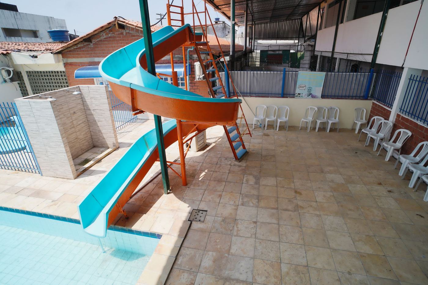 Toboágua azul e laranja descendo até a piscina, com área de cadeiras ao redor
